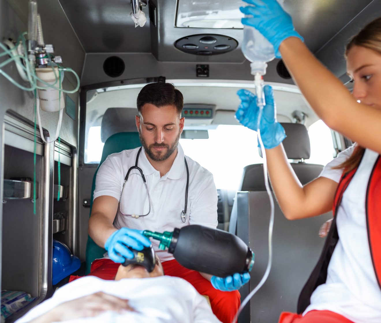 View from inside ambulance of uniformed emergency services workers caring for patient on stretcher during coronavirus pandemic.